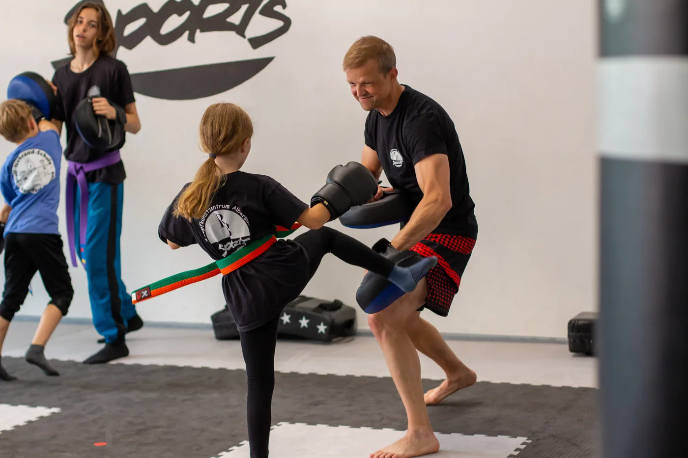 Mädchen tritt im Thaiboxen-Training gegen das Schlagpolster des Trainers