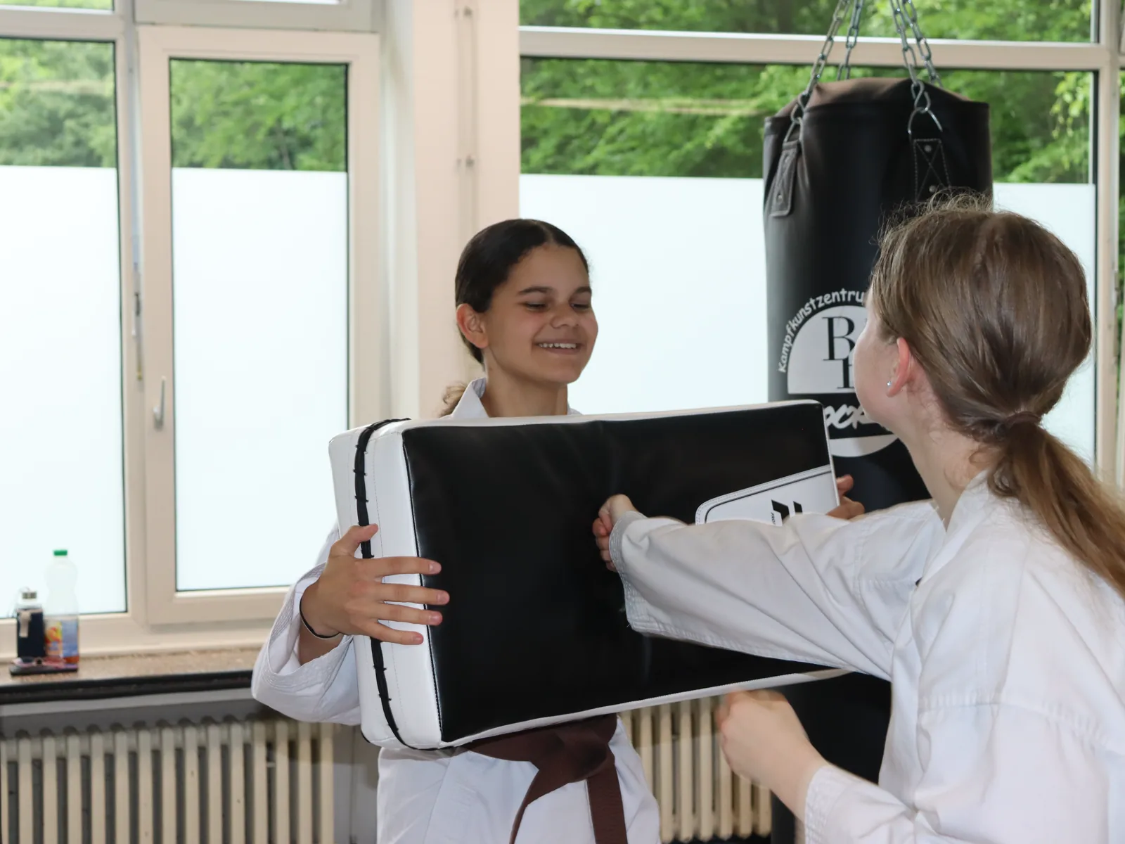 Zwei Jugendliche halten sich lachend das Schlagpolster beim Partnertraining