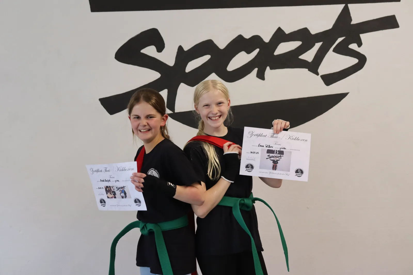 Zwei Jugendliche zeigen stolz ihr Thai-/Kickbox-Zertifikat und den grünen Gürtel