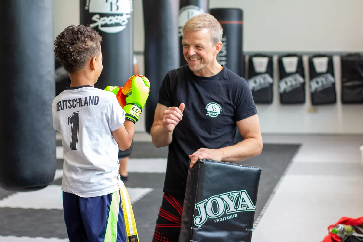 Trainer lacht mit einem Kind mit Boxhandschuhen