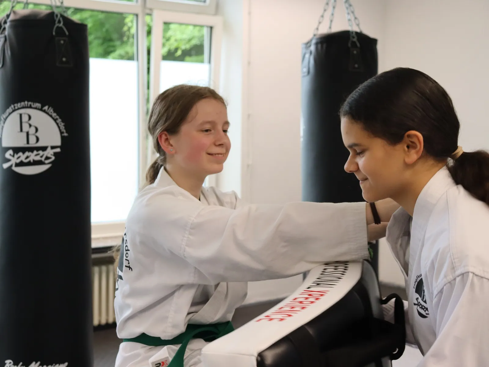 Zwei Mädchen halten sich im Partnertraining lachend gemeinsam das Schlagpolster