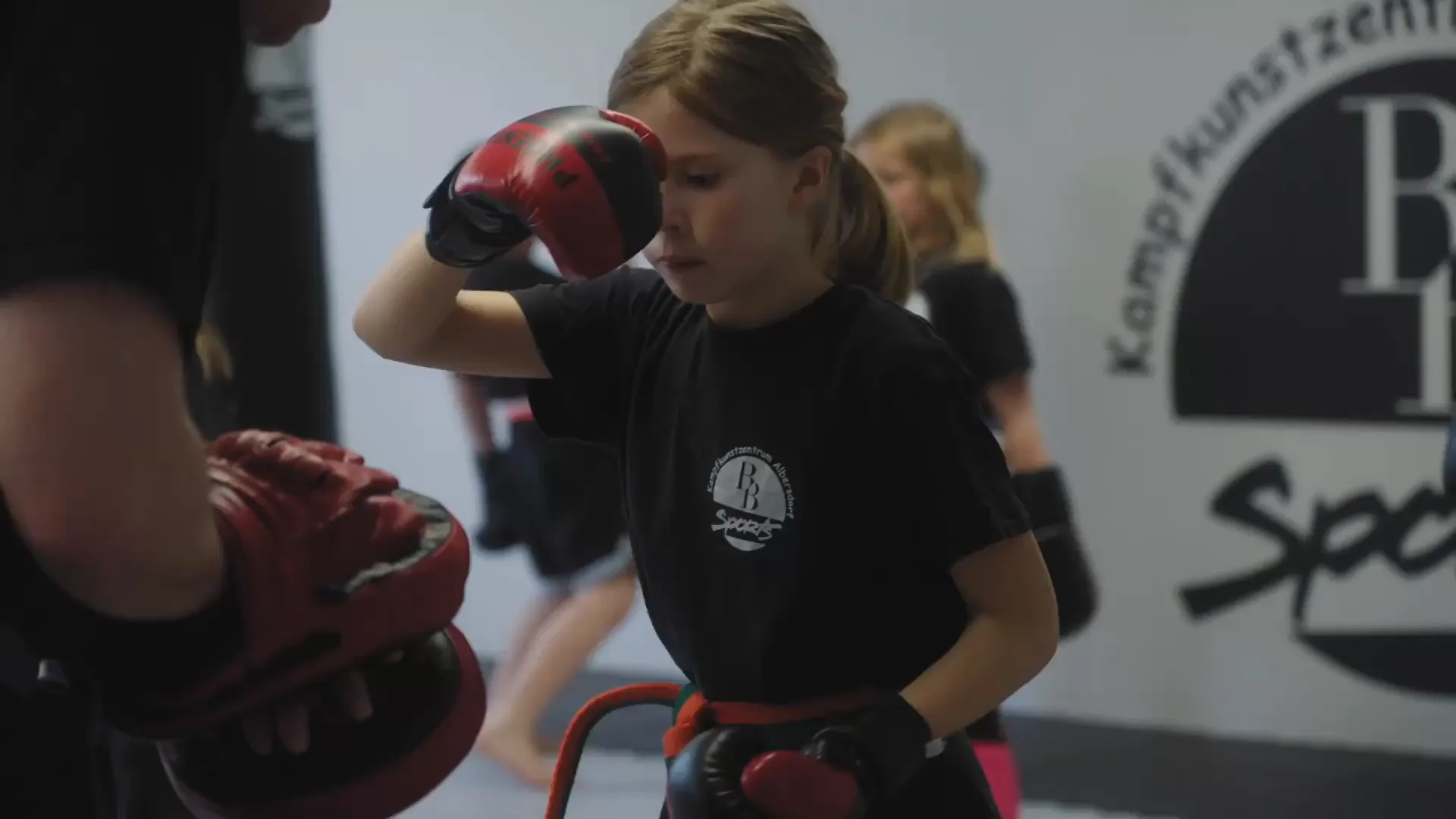 Mädchen mit Boxhandschuhen schlägt im Training auf die Pratze des Trainers
